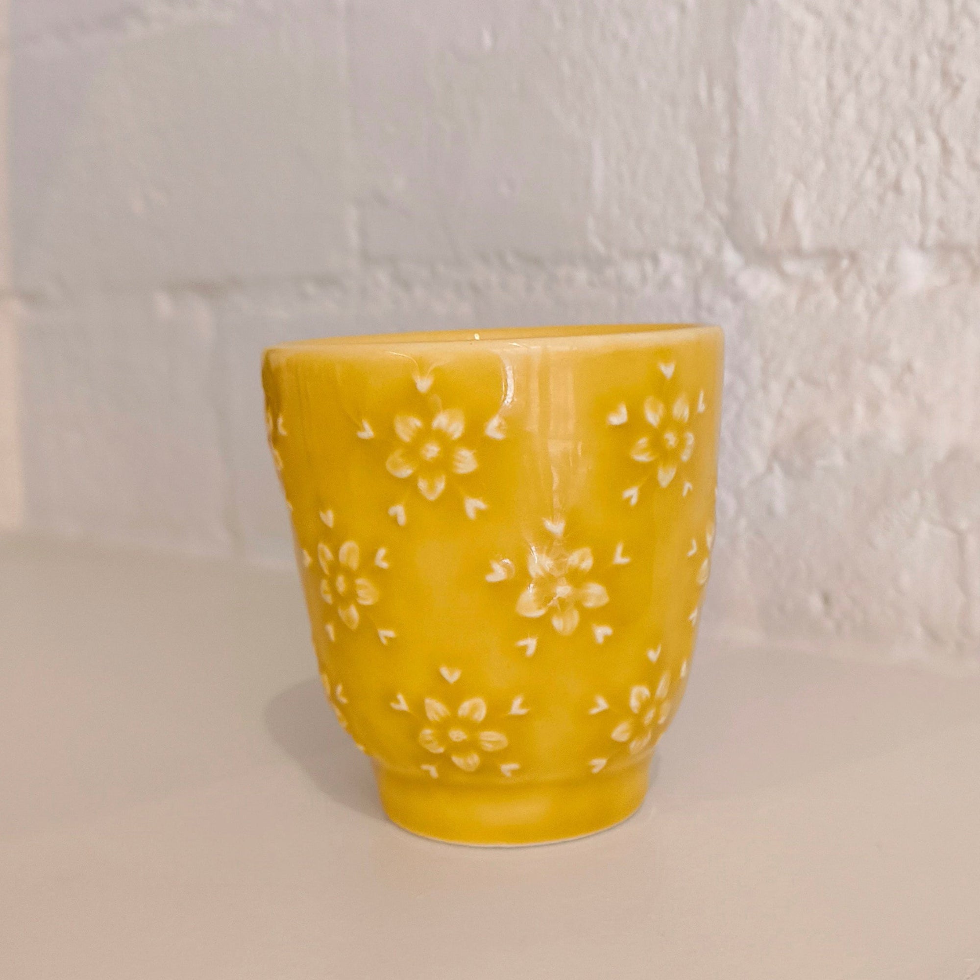 Yellow ceramic cup with floral patterns on a white countertop against a light tiled wall.
