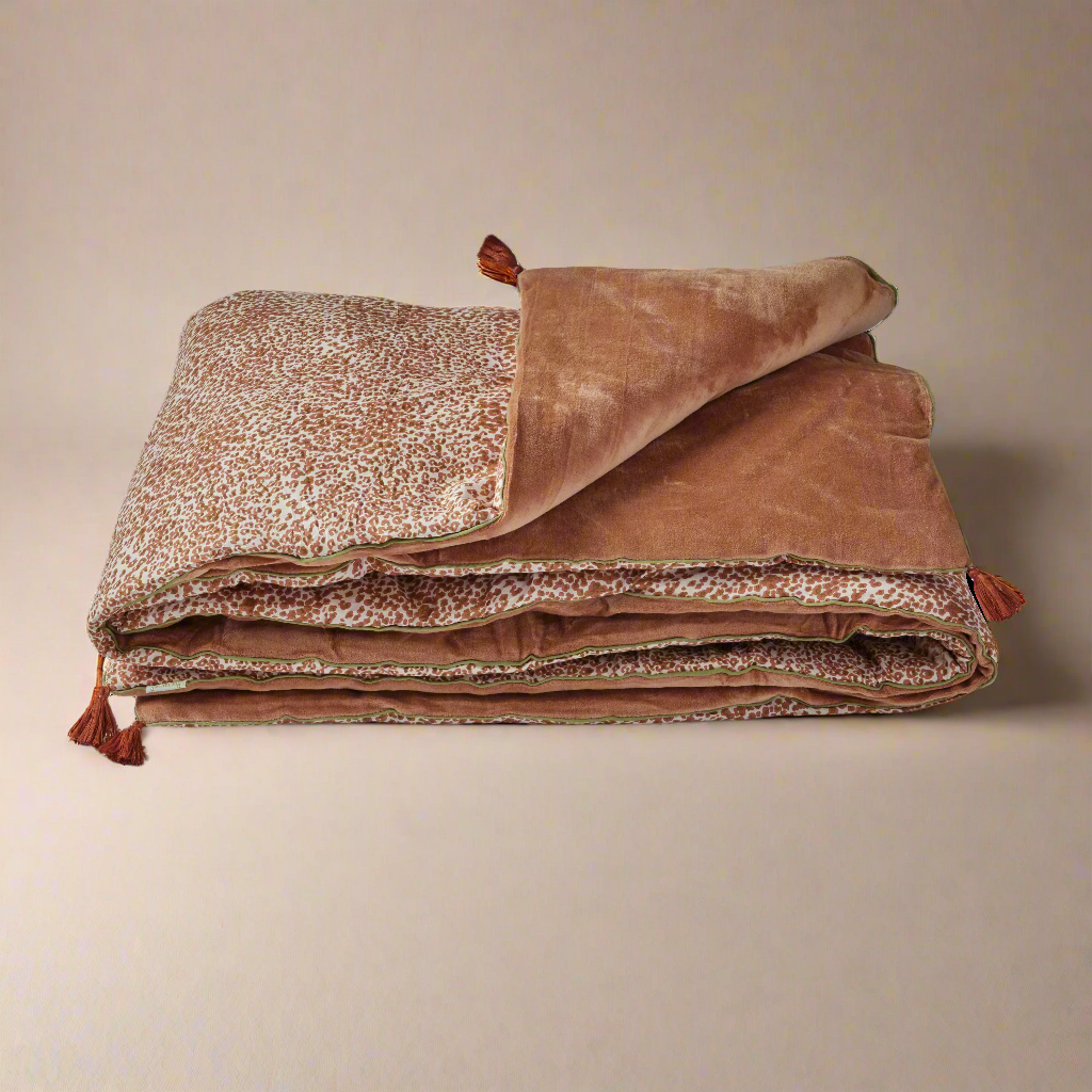 A folded sofa cover with a bohemian terracotta color and a floral print on one side, revealing a soft velvet texture on the other side.