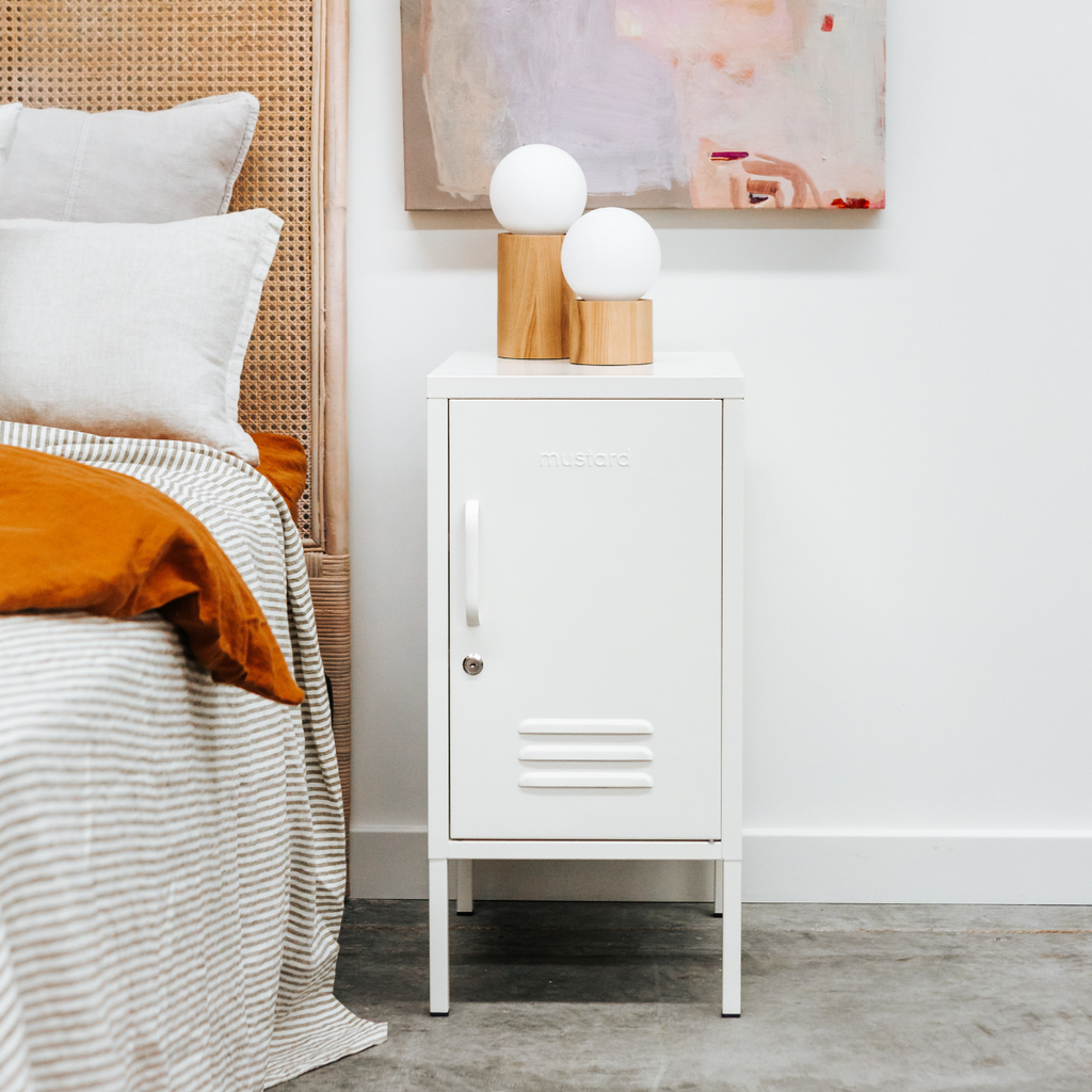 White locker-style nightstand next to a bed with white bedding and orange blanket.