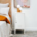 White locker-style nightstand next to a bed with white bedding and orange blanket.