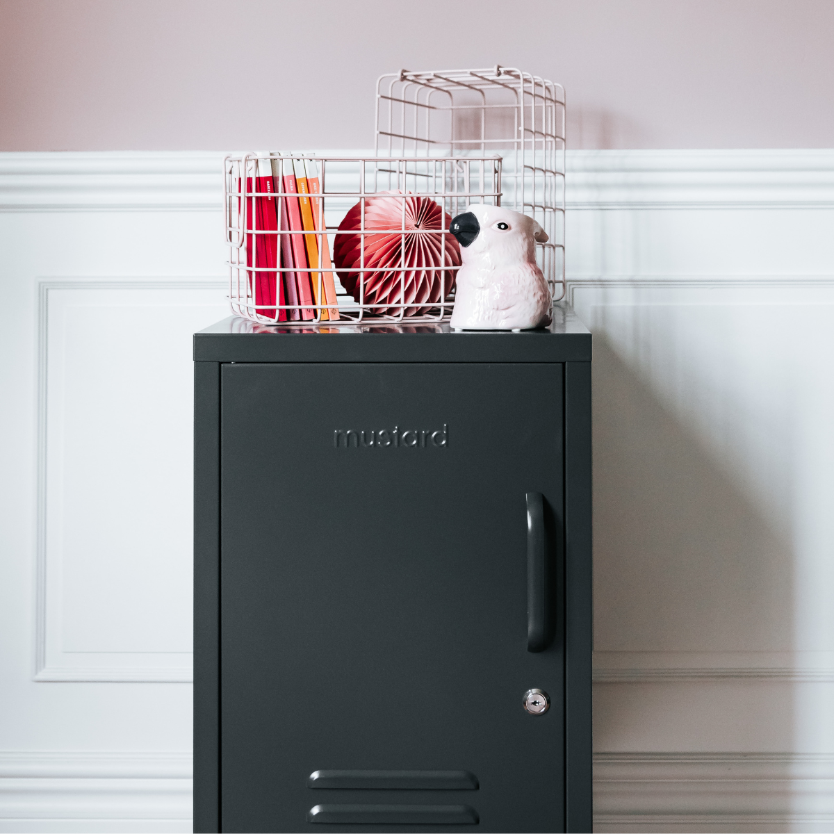 Black locker with a wire basket on top containing colorful items against a white wall.