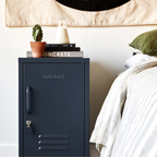 Slate nightstand with 'Muji' branding next to a bed with green pillow and white bedding.