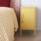 Yellow metal cabinet next to a bed with striped bedding and a red pillow.