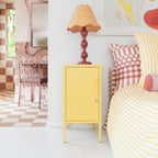 Yellow cabinet with a lamp next to a bed with striped bedding and checkered pillows.