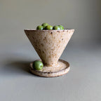 Ceramic bowl with a funnel shape containing green olives on a gray surface.