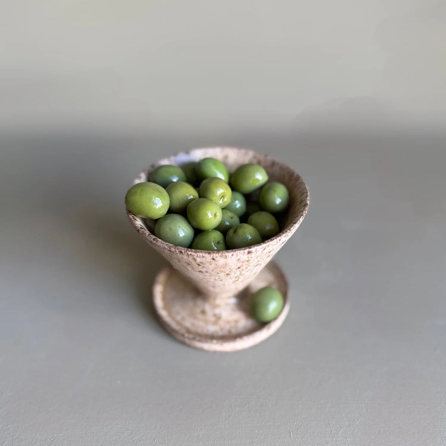 Small ceramic bowl filled with green grapes on a light gray surface