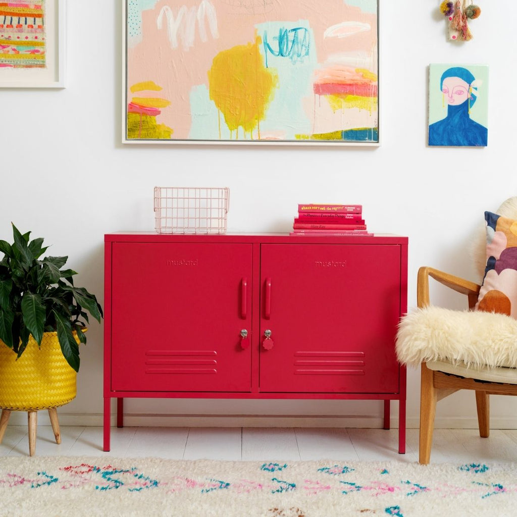 Red cabinet in a room with colorful abstract art and a plant.