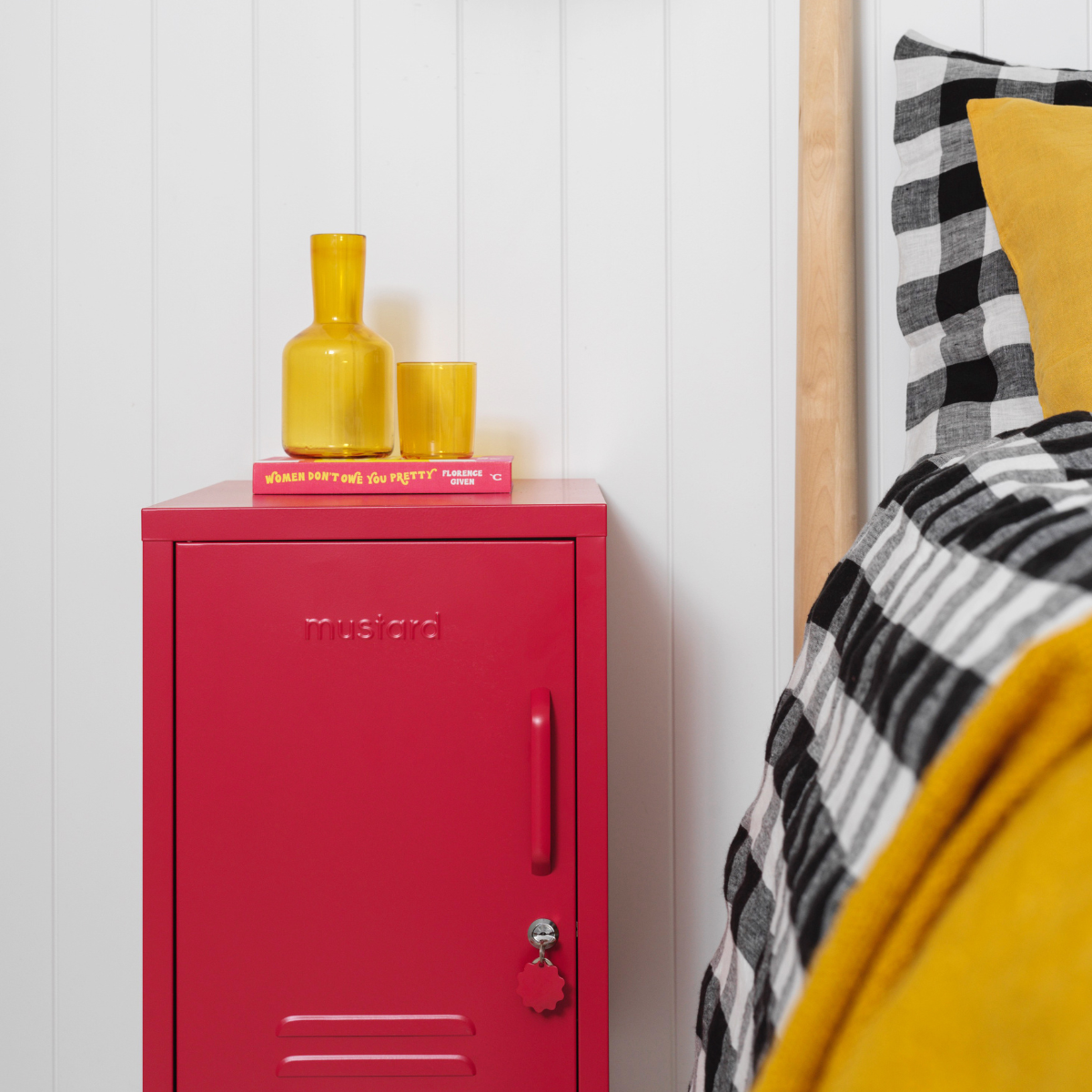 Red locker with yellow bottles on a white wall next to a bed with checkered pillows.