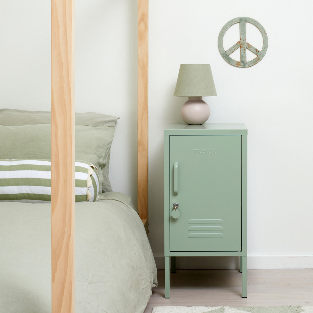 Sage metal locker bedside table with lamp on next to a bed
