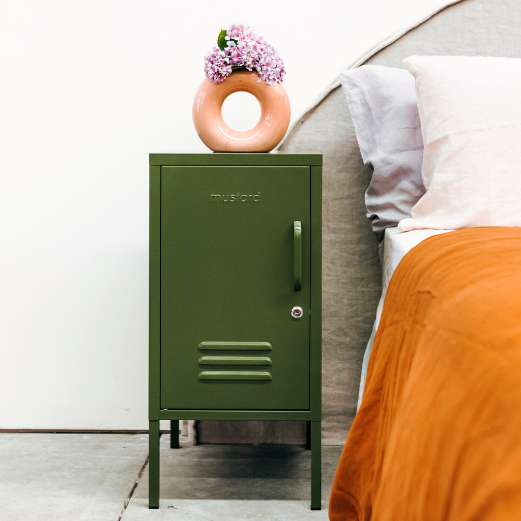 Olive metal locker with a circle vase and flowers on top next to a bed