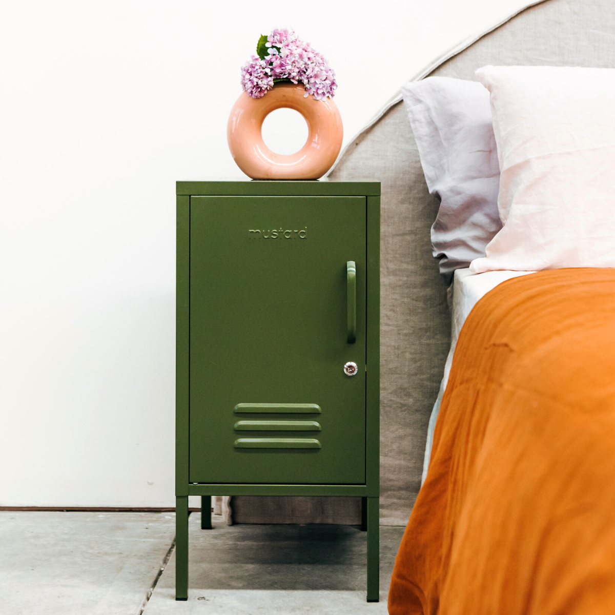 Olive metal locker with a circle vase and flowers on top next to a bed