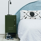 Green metal locker next to a bed with a decorative pillow featuring an eye design.