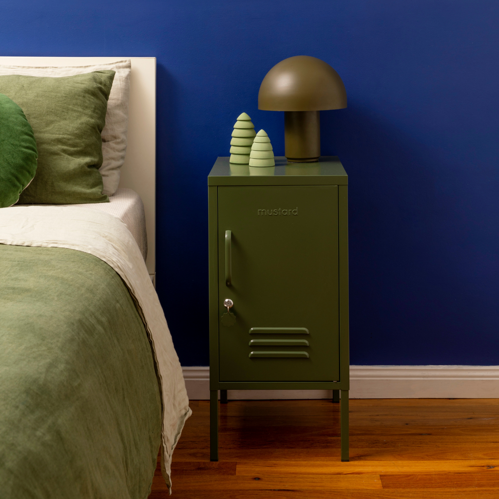 Green nightstand with decorative items next to a bed against a blue wall