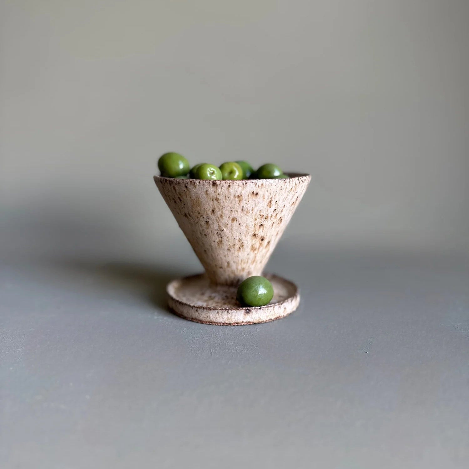 Small ceramic bowl with speckled texture filled with green olives on a plain background