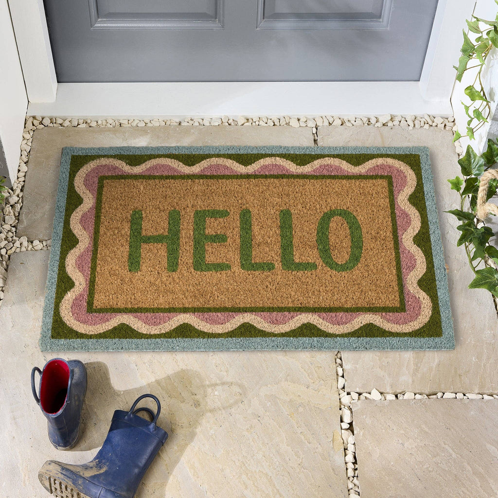 Doormat with 'HELLO' text on a stone porch with shoes and a plant.