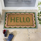 Doormat with 'HELLO' text on a stone porch with shoes and a plant.