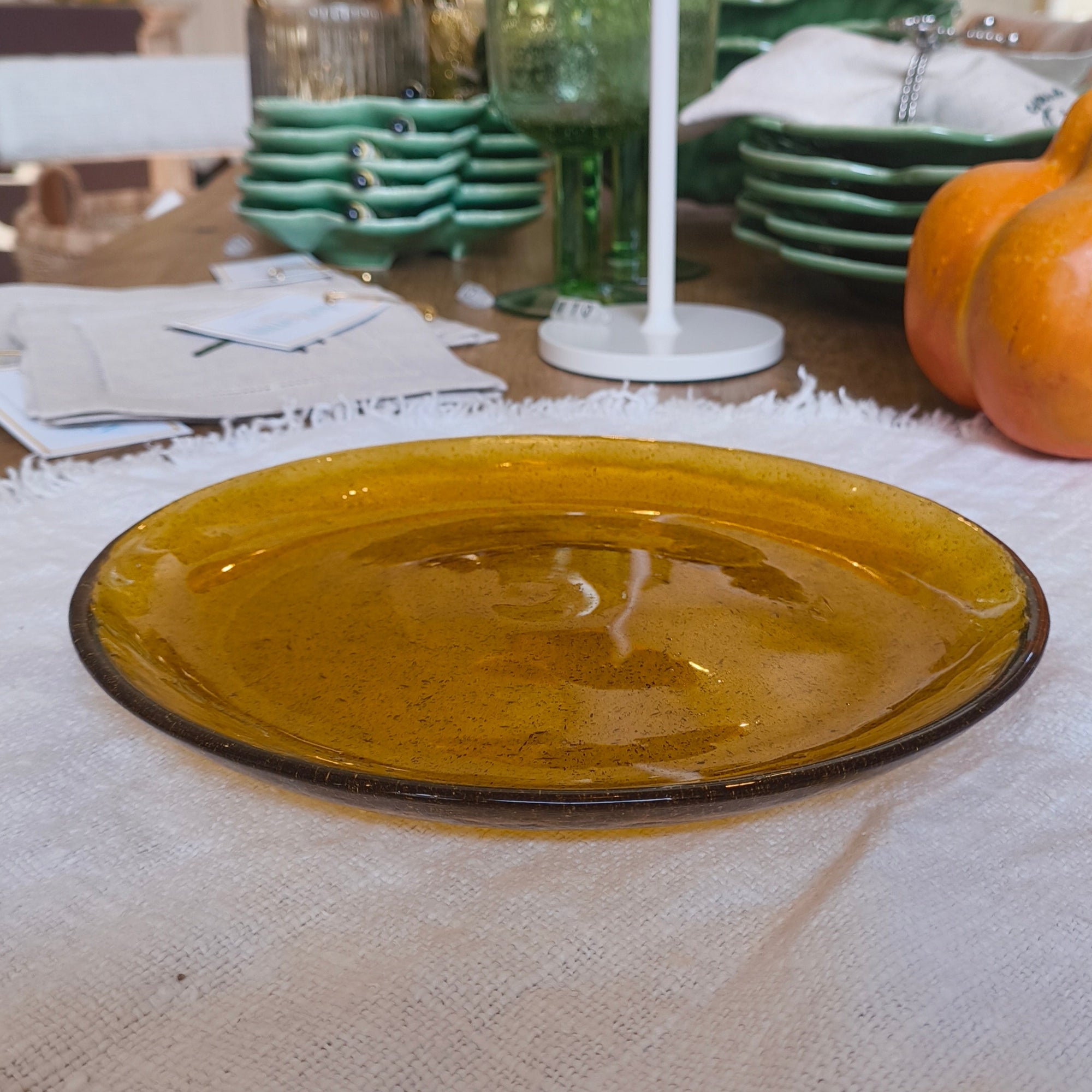 Amber coloured glass plate on a white textured tablecloth with pumpkins and decorative items in the background.