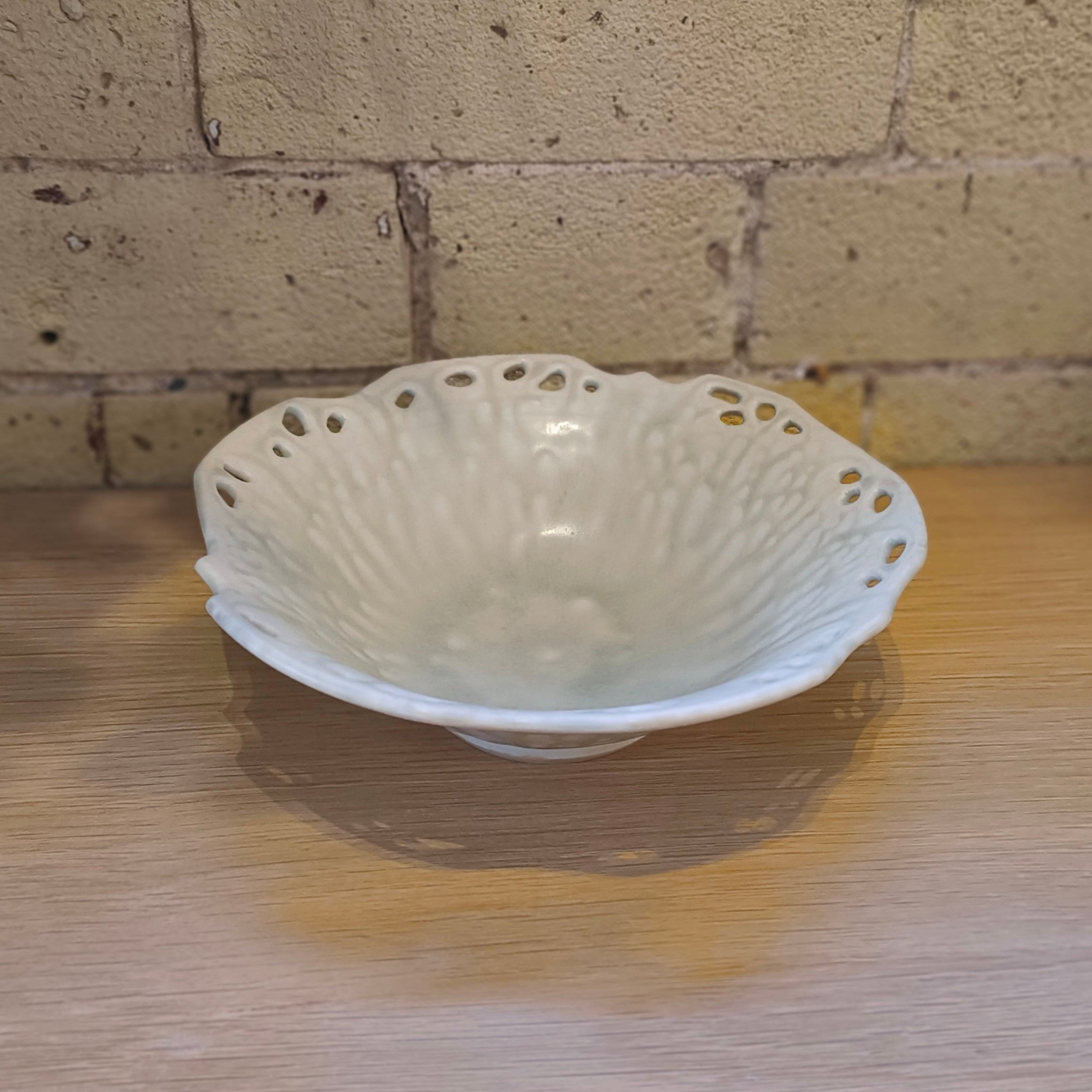 White ceramic bowl with decorative pattern on a wooden surface with a brick wall background