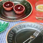 Plates with cut blood oranges and a glass of juice on a checkered tablecloth.