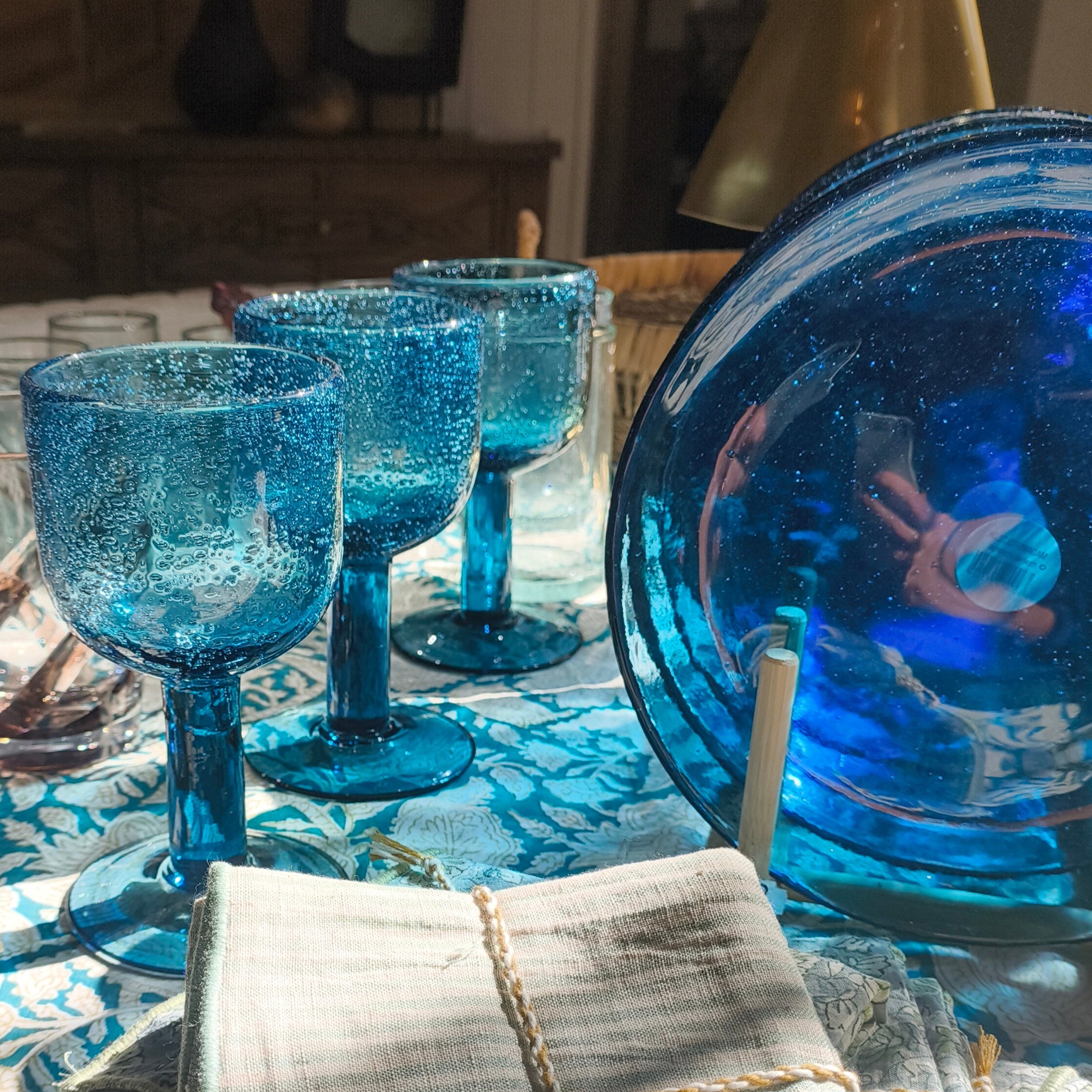 Dining table set with blue glassware and a patterned tablecloth.