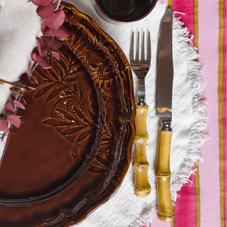 Dinner setting with brown plates, white napkins, and decorative elements on a pink and gold striped tablecloth.
