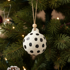 White spherical ornament with black polka dots hanging on a white background