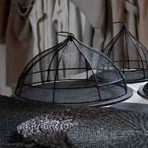 Black wire cloche lids on a surface with beige aprons hanging in the background.