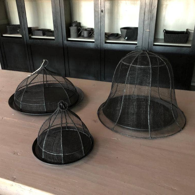 Three black wire mesh cloches on a wooden surface with a blurred background.