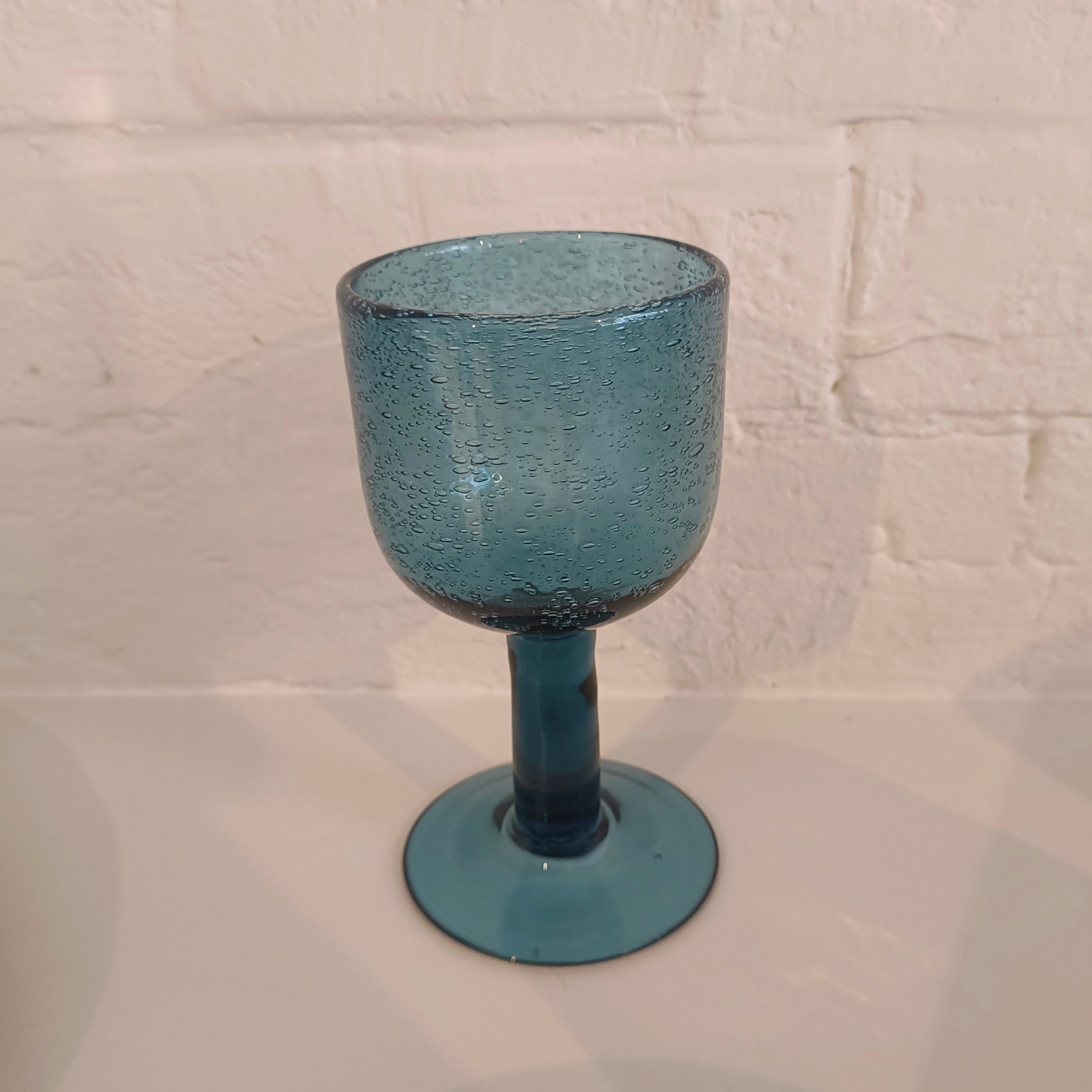Blue textured glass goblet on a white tiled surface