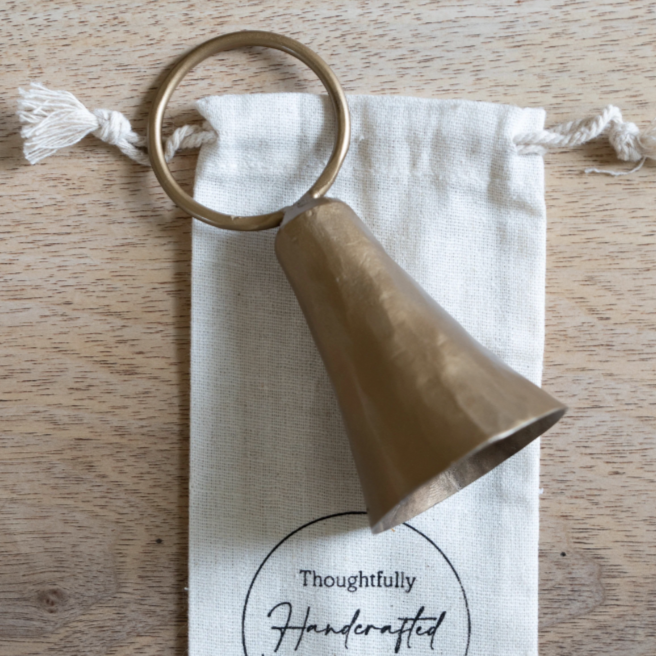 Brass bell on a branded drawstring bag on a wooden surface