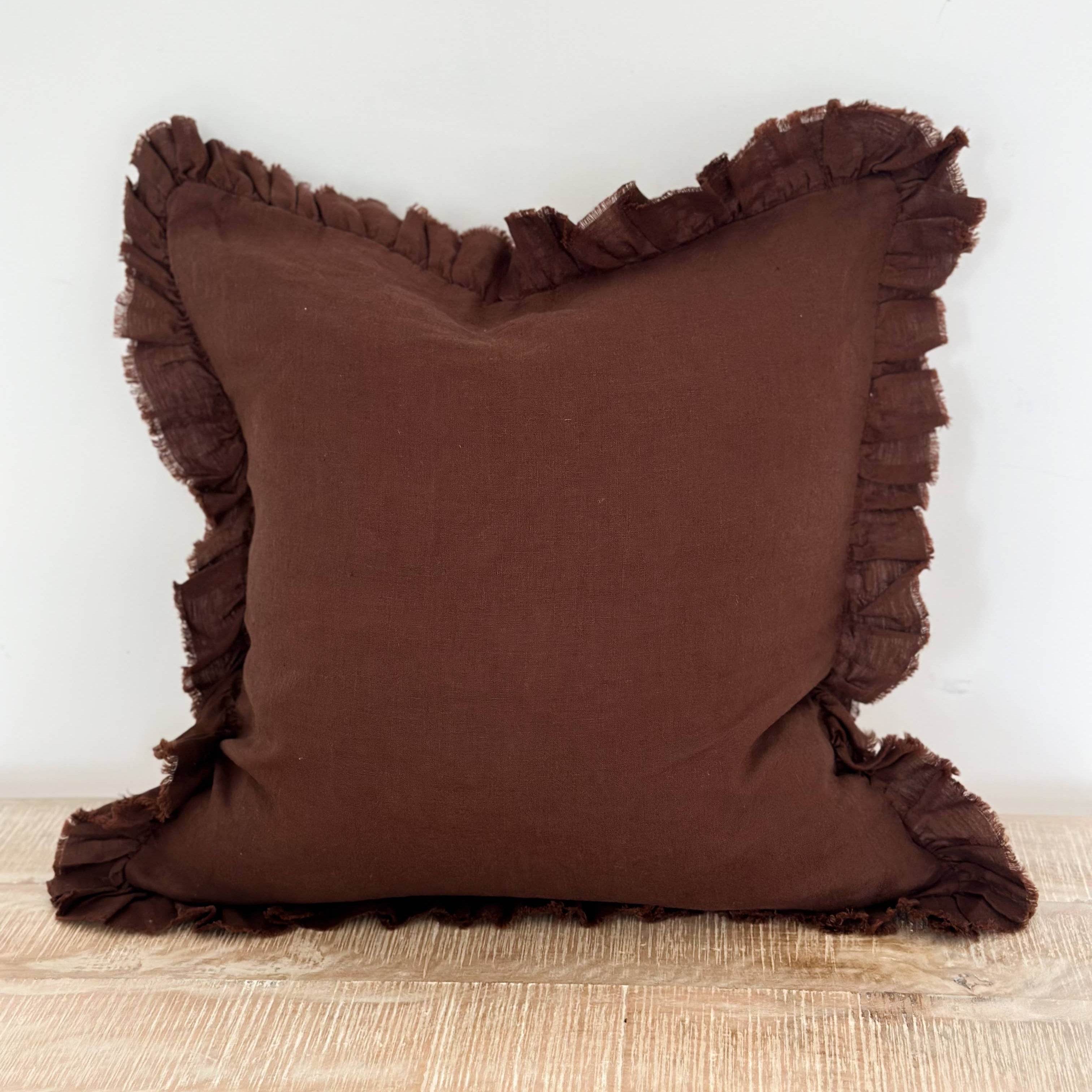 Brown pillow with ruffled edges on a wooden surface and white background