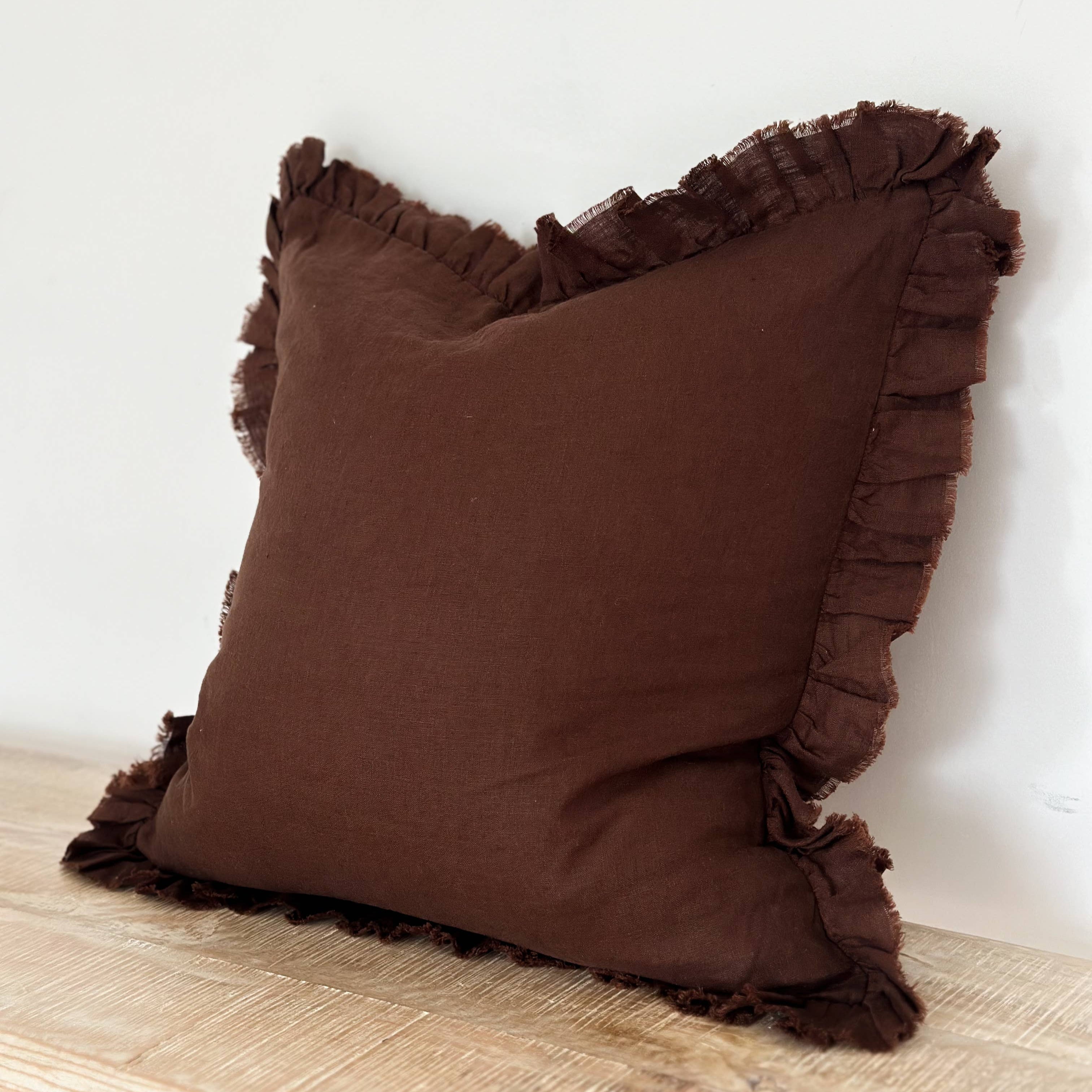 Brown pillow with ruffled edges on a wooden surface against a white wall