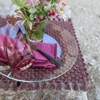 Table setting with a glass plate, pink napkin, and floral arrangement on a textured surface.