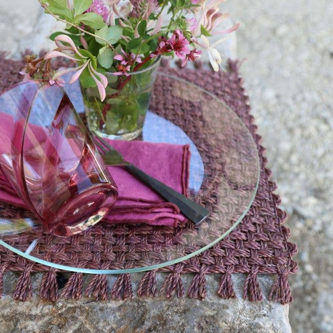 Table setting with a glass plate, pink napkin, and floral arrangement on a textured surface.