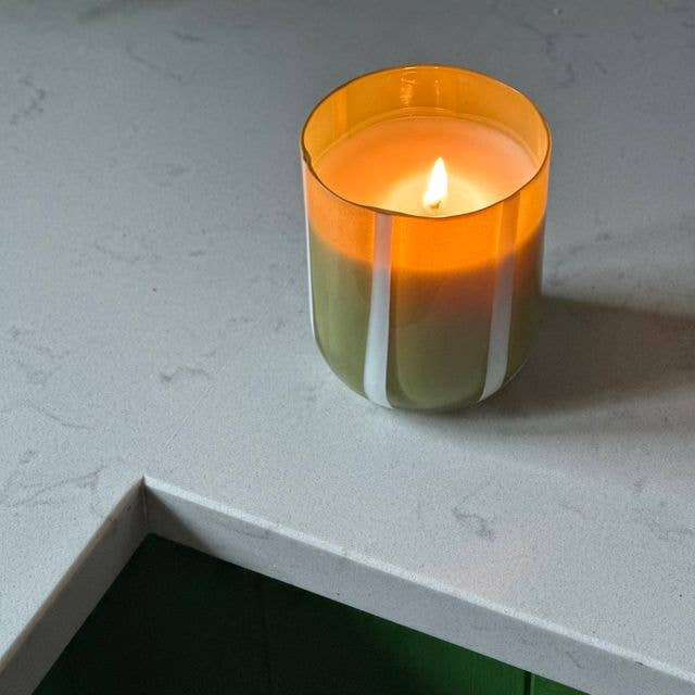 Candle in an orange glass holder on a white surface