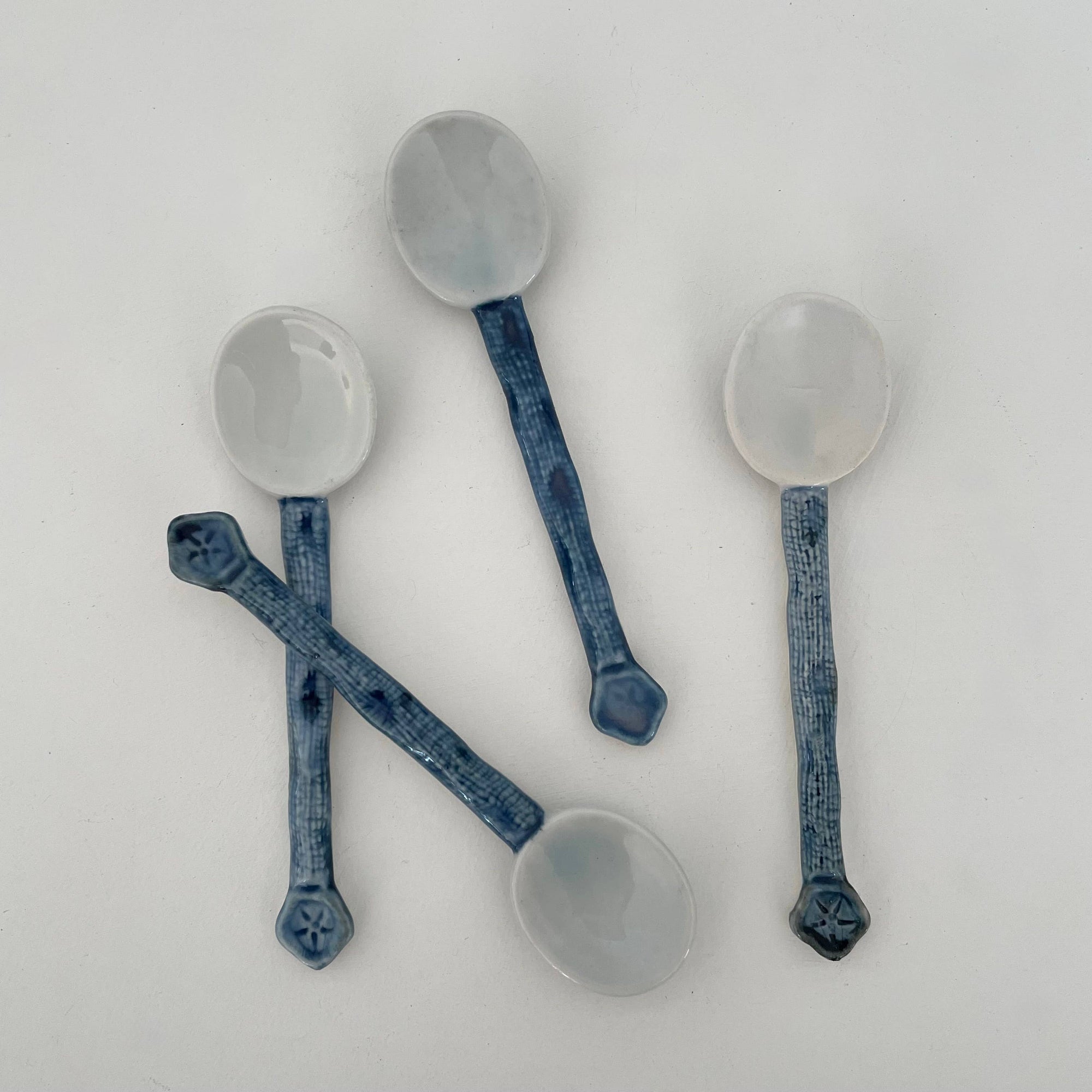 Set of four ceramic spoons with blue handles on a white background