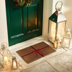 Decorative doormat with a red bow on a stone floor in front of a green door, surrounded by lanterns.