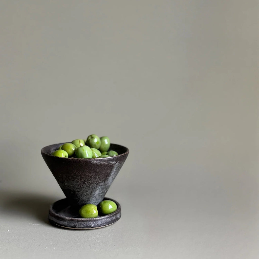 Small dark ceramic bowl with green apples on a light gray background