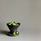 Small dark ceramic bowl with green apples on a light gray background