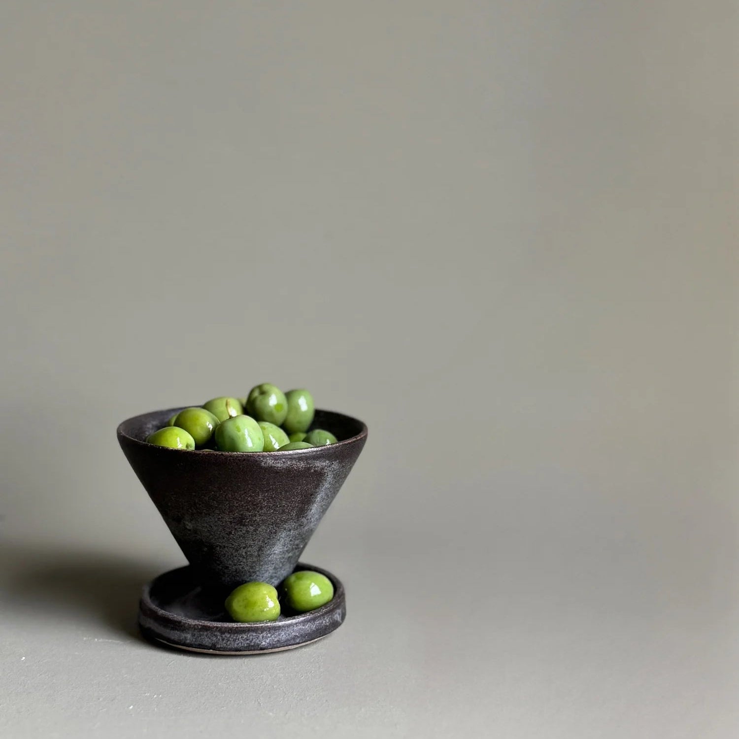 Small dark ceramic bowl with green apples on a light gray background