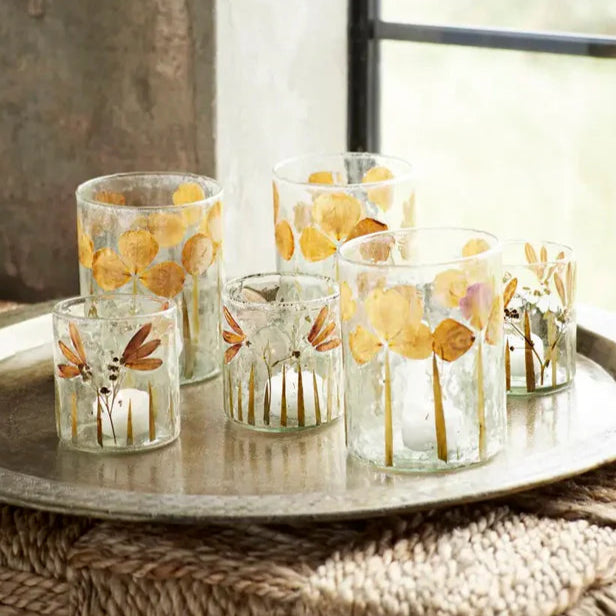 Set of glass candle holders with floral designs on a wooden surface.