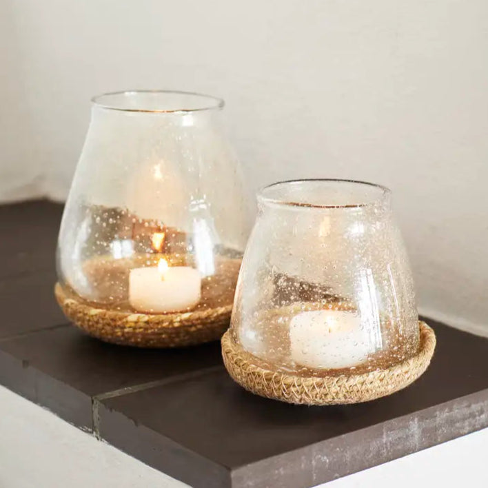 Two glass candle holders with candles on a dark surface.