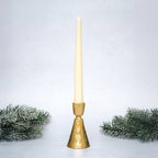 Gold candle holder with a white candle on a light gray background with decorative greenery.