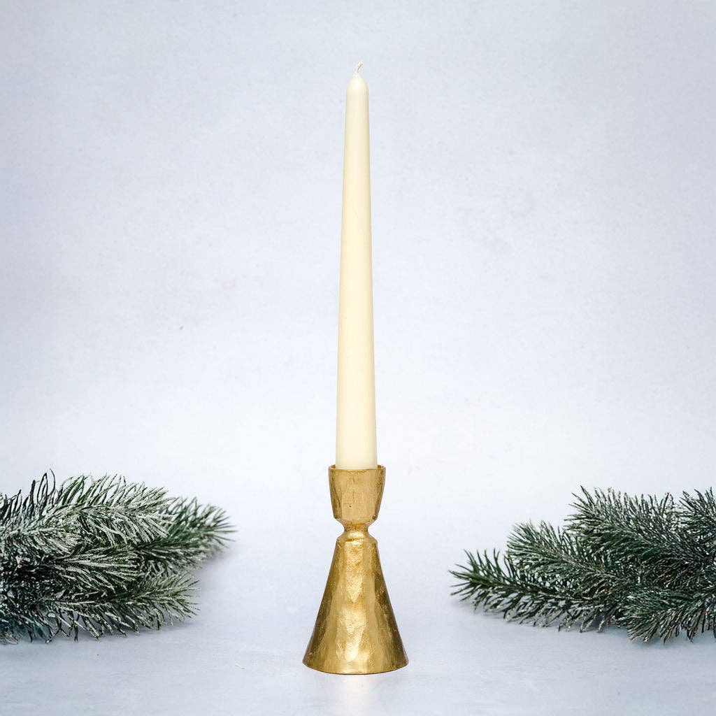 Gold candle holder with a white candle on a light gray background with decorative greenery.