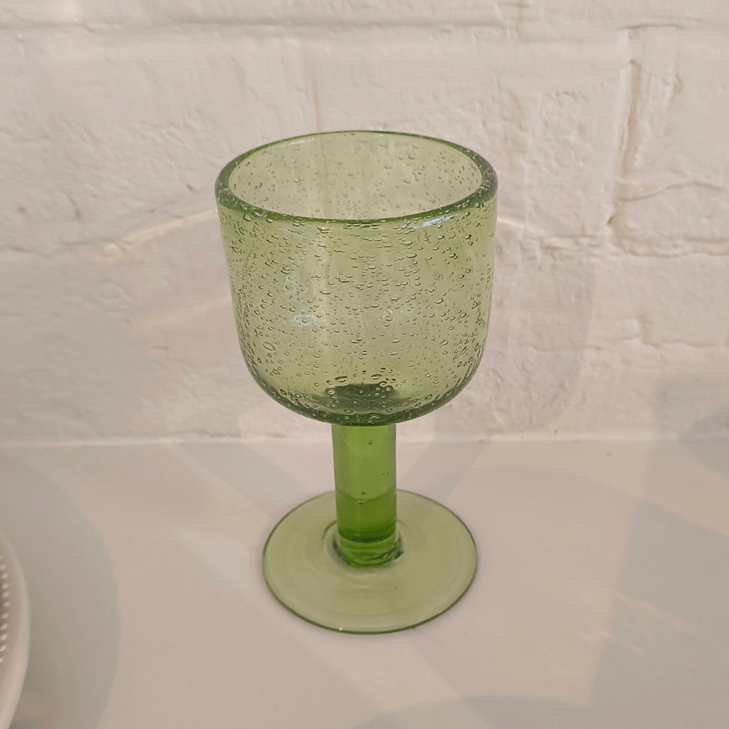 Green glass goblet on a white surface with a white brick wall background