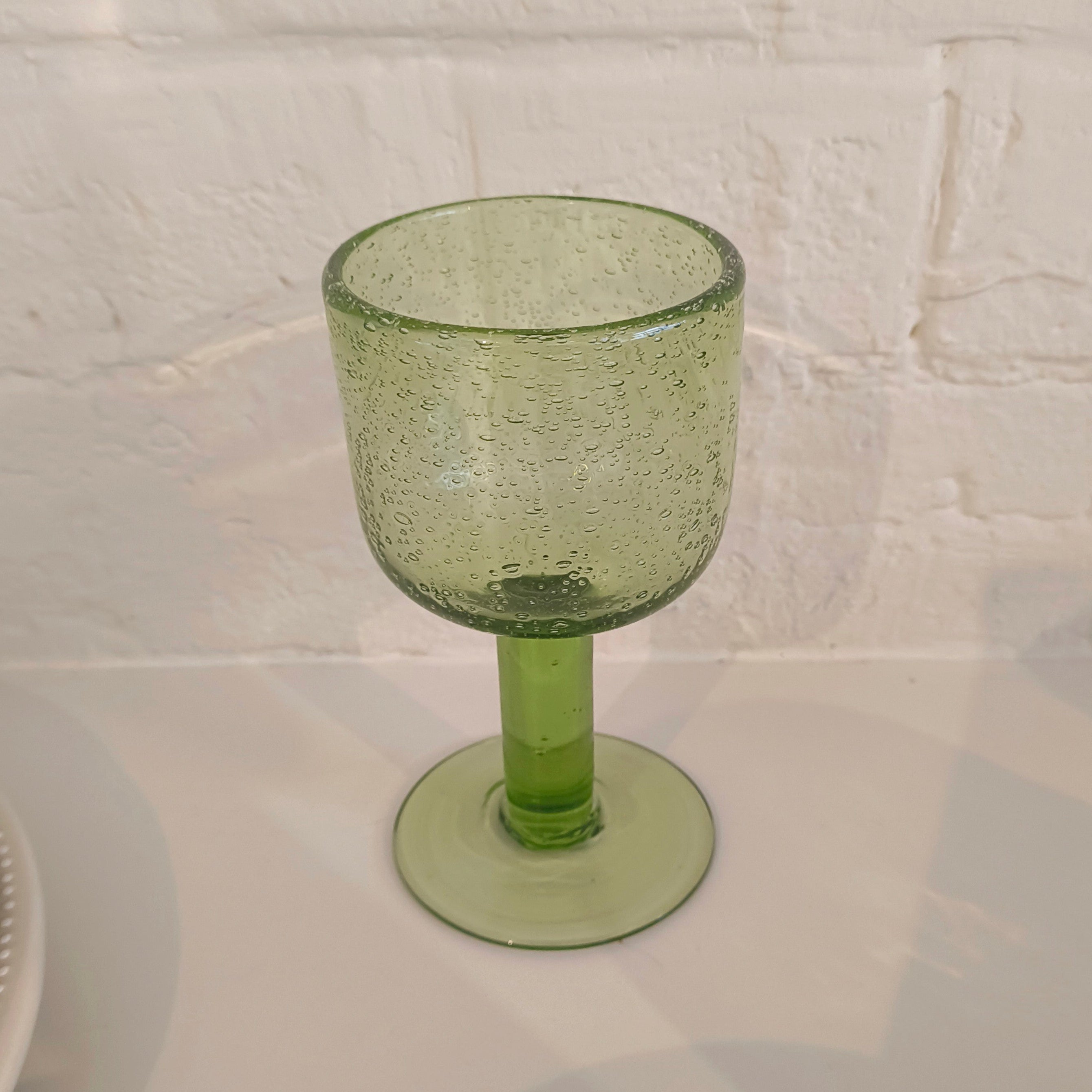 Green glass goblet on a white surface with a white brick wall background