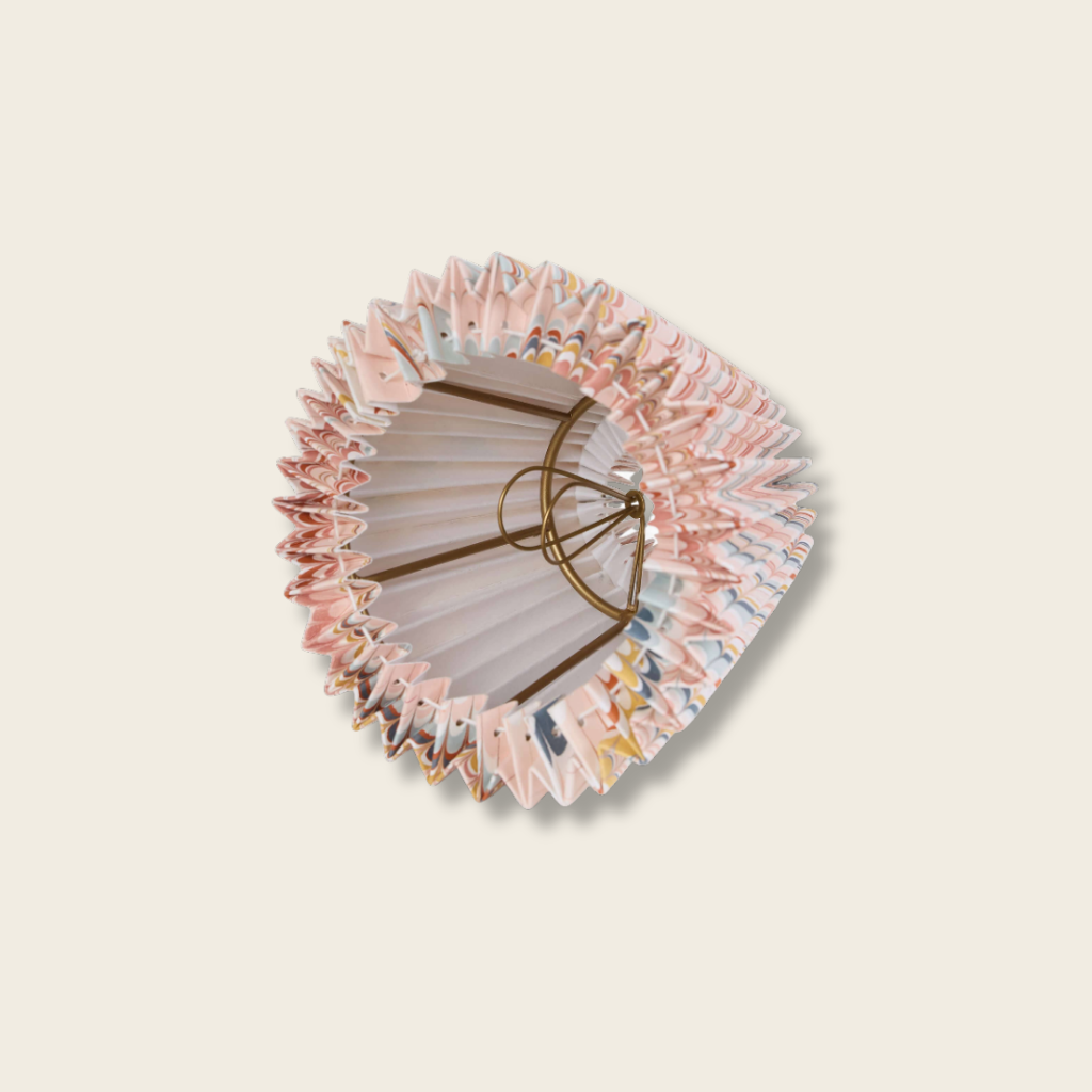 inside detail of a pleated lampshde woth brass wire clip on beige background
