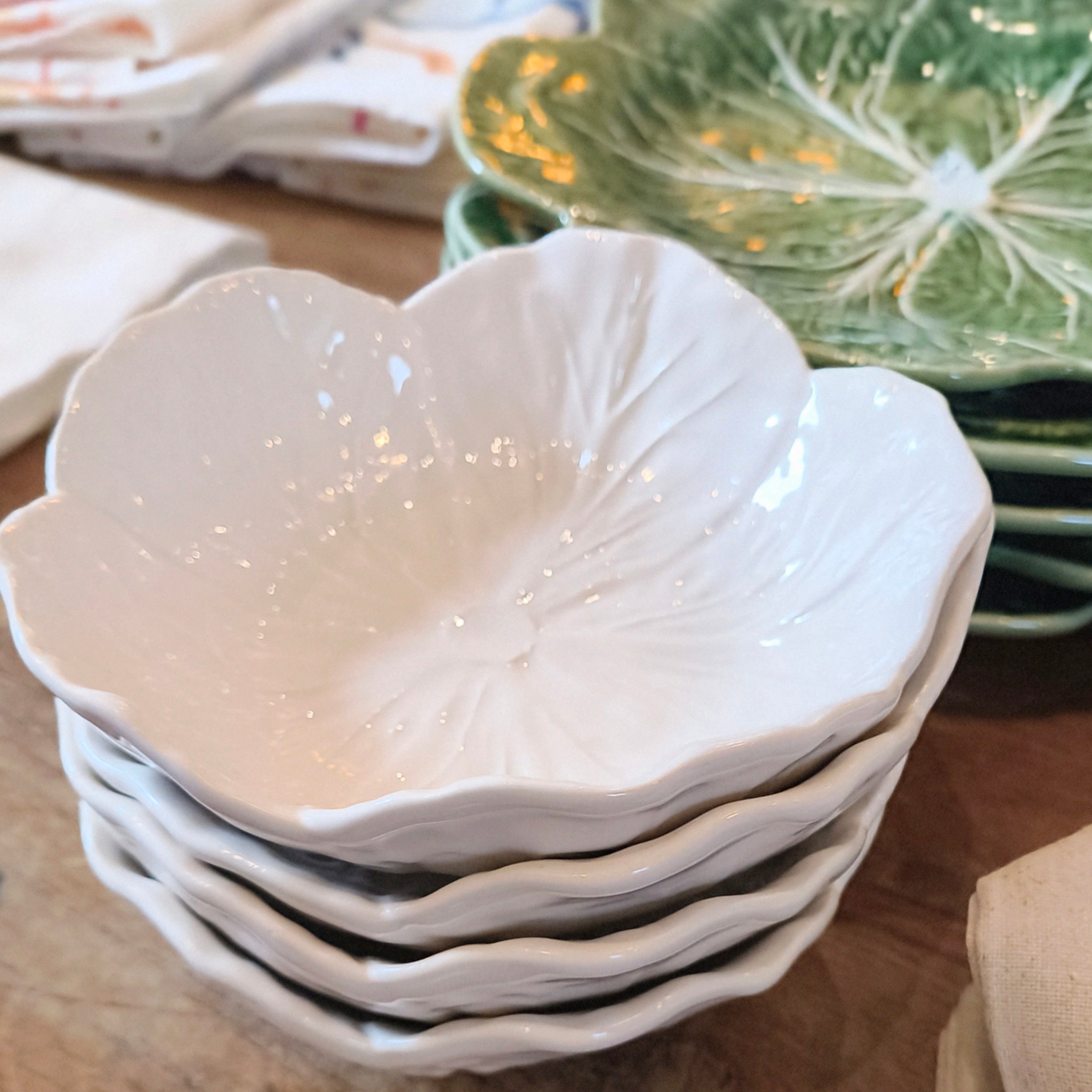 Stack of white ceramic leaf-shaped bowls on a wooden surface with green leaf-patterned plates in the background.