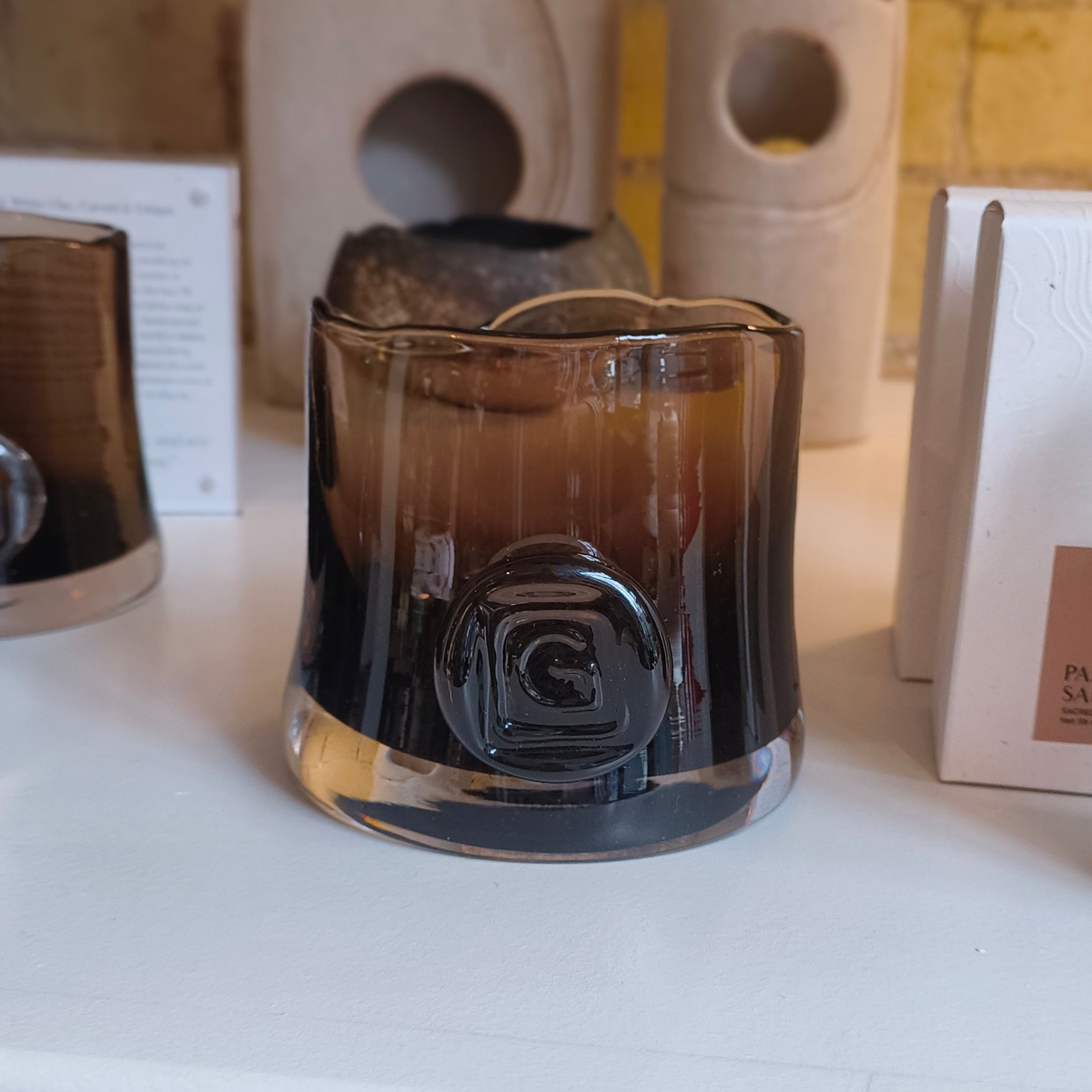 Decorative items including a glass candle holder and a bottle on a white surface with a brick wall background.