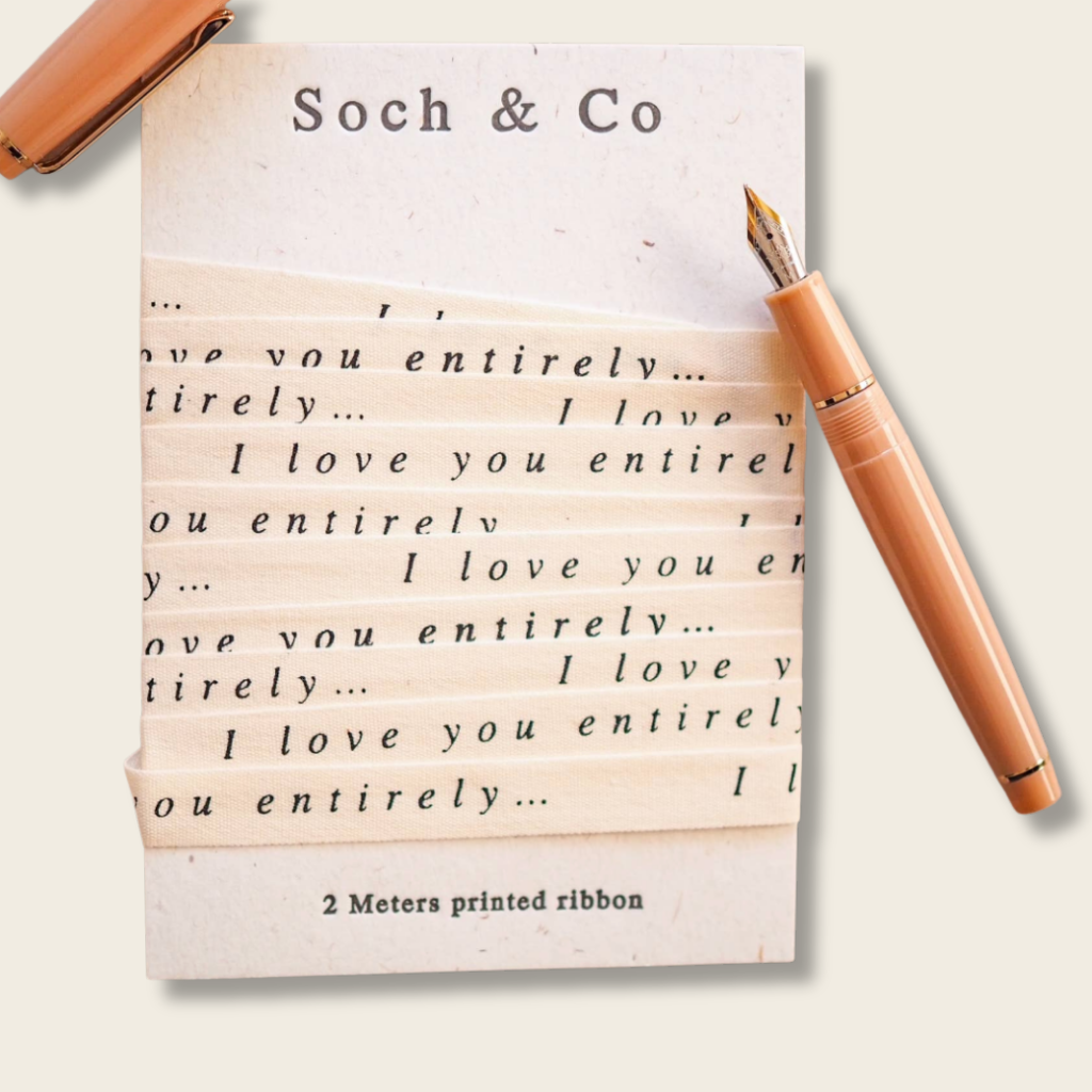 Printed ribbon with 'I love you entirely...' text and a matching pen on a beige background.